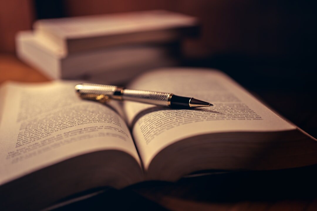 Antique quill pen resting on an open book beside an inkwell on a dark wooden table