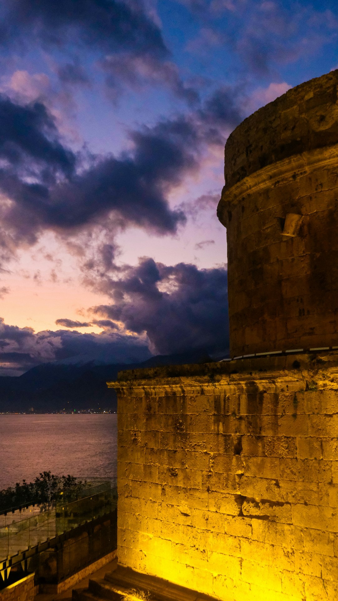 Old stone coastal town illuminated at night with warm lights reflecting on the sea